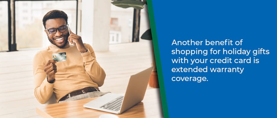 Another benefit of shopping for holiday gifts with your credit card is extended warranty coverage - Image of a man with his laptop open holding his credit card and talking on his cell phone